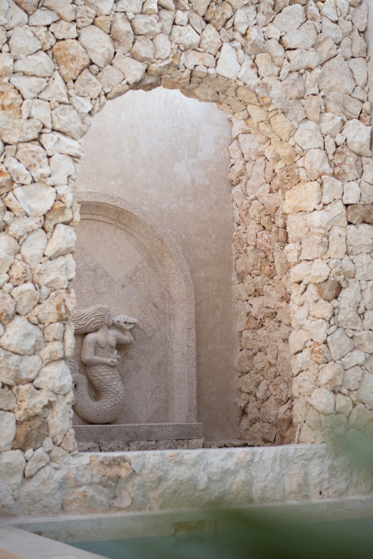 Carved stone archway with a mermaid relief above a pool