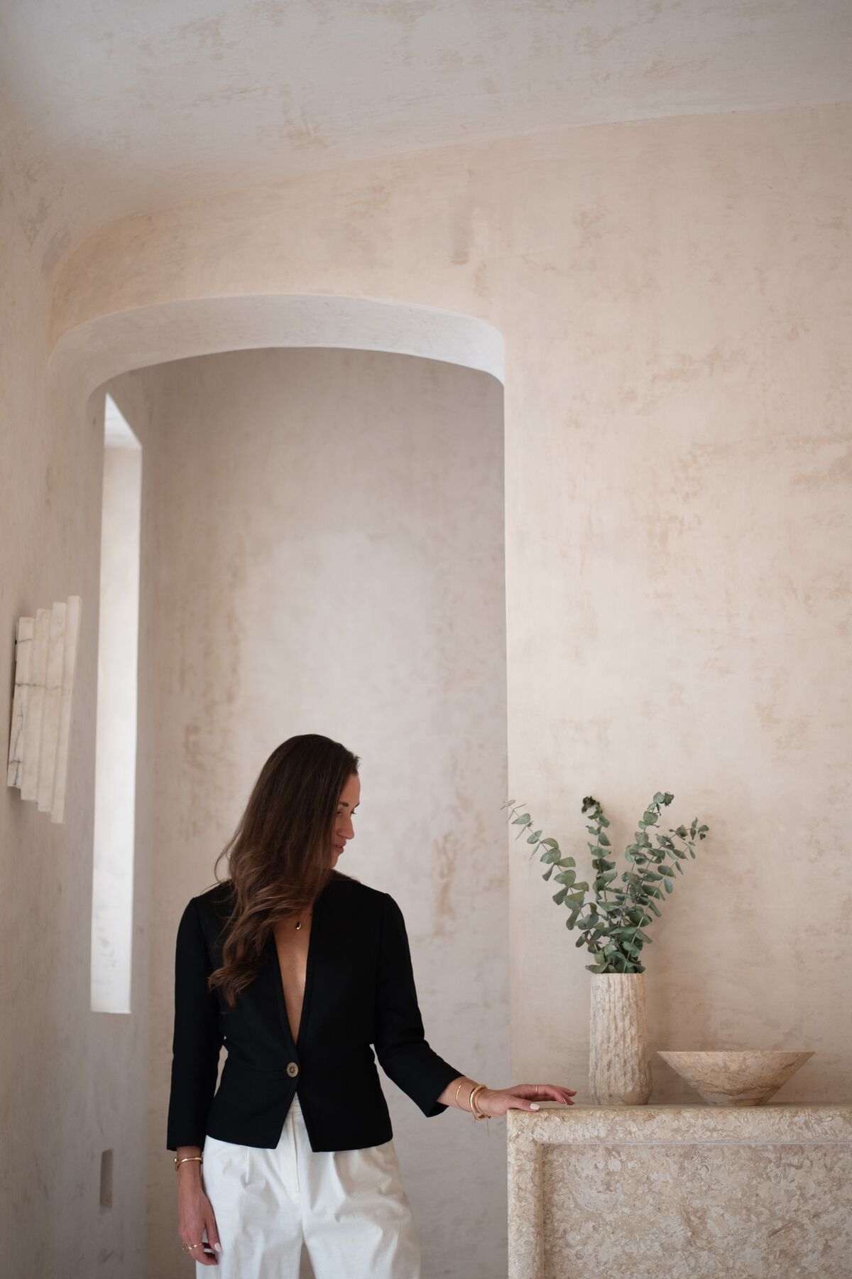 Woman in a black blazer standing in a sunlit plaster alcove